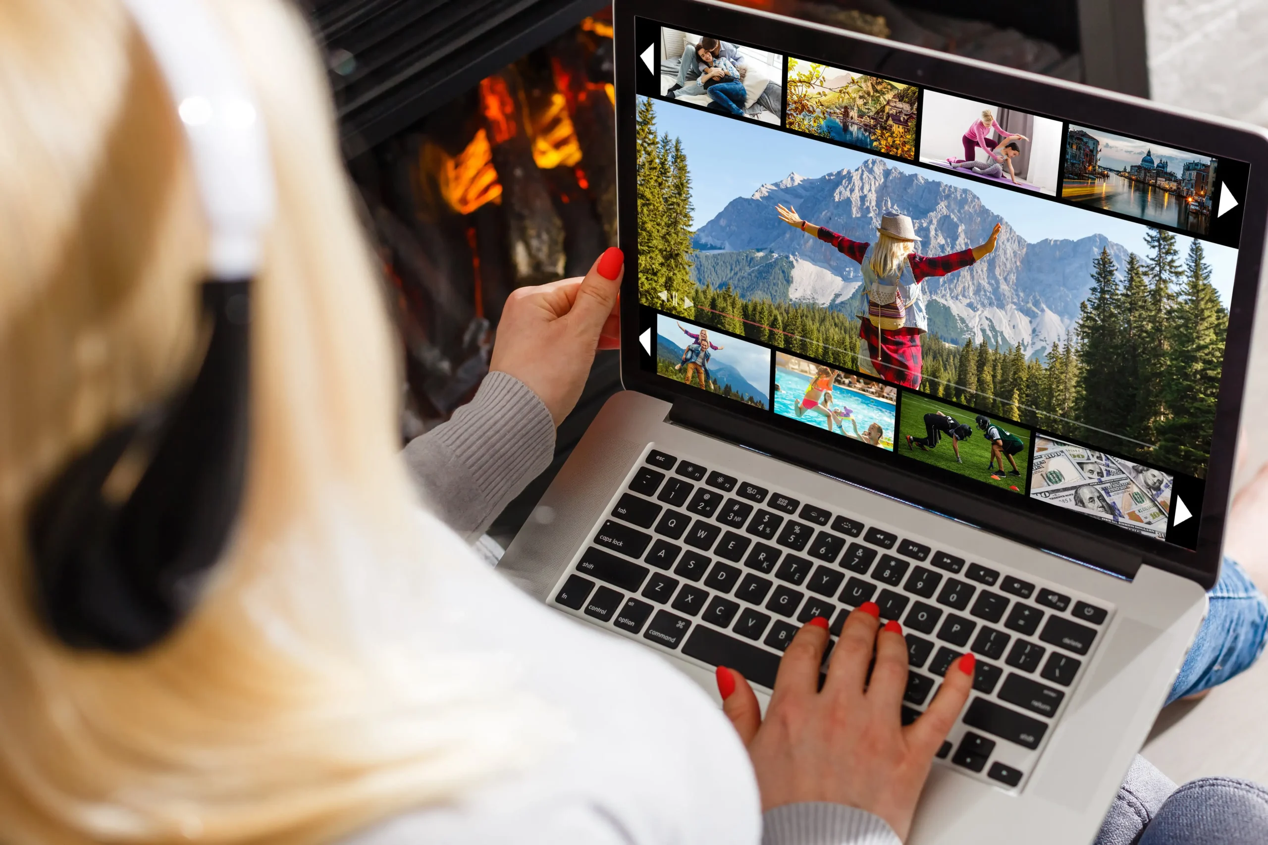 Close-up of a woman using a laptop to view travel and family photos while sitting near a fireplace