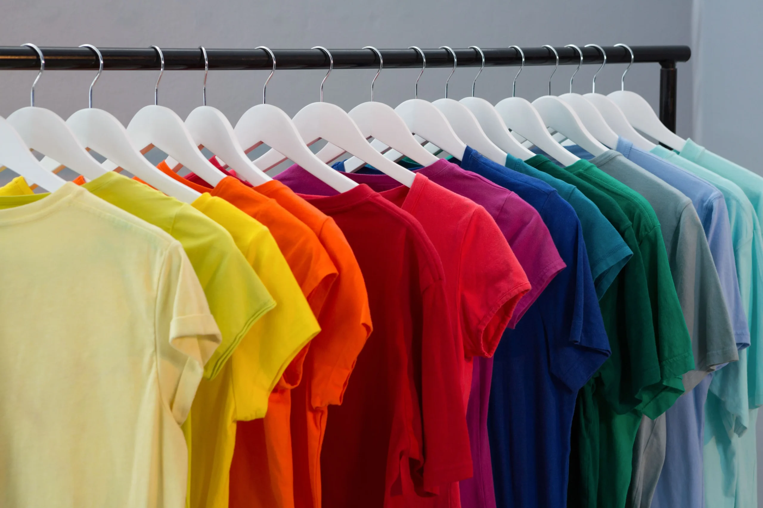 Row of plain T-shirts in various colors arranged on white hangers on a metal clothing rack